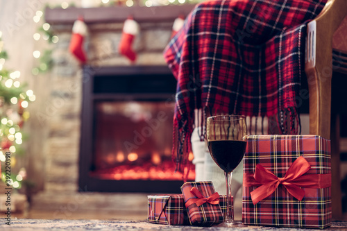 Legs of disabled woman in a socks covered plaid sitting and relaxation on armchair near fareplace and christmas tree with glass of wine after finishing pakking gift boxes for family. Bottom view.