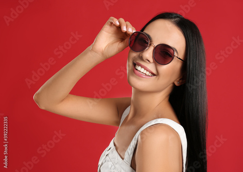 Beautiful woman wearing sunglasses on red background