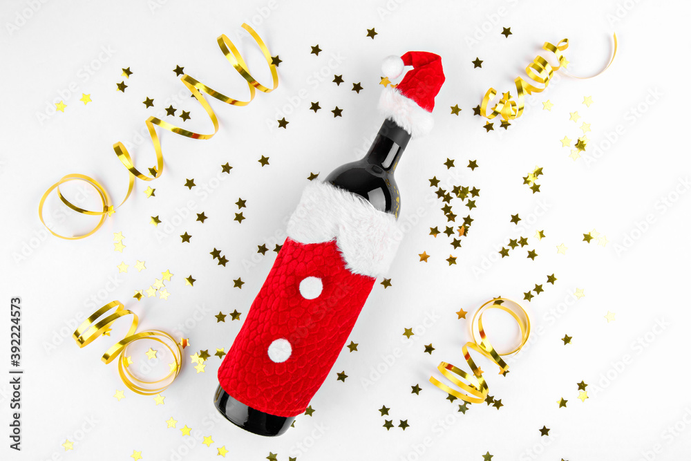 Christmas wine bottle wearing a Santa hat and Santa dress top view on white background with Christmas golden festive decoration. Merry Christmas and New Year congratulation