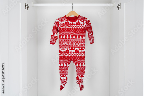 White and red christmas pajamas hanging on a wooden hanger in the middle of a white closet.