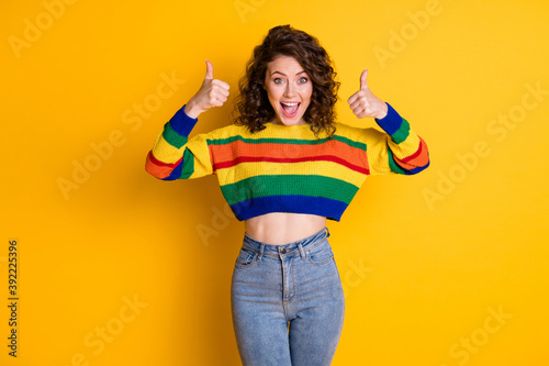 Photo portrait of cute girl raising two thumbs up with open mouth isolated on bright yellow colored background