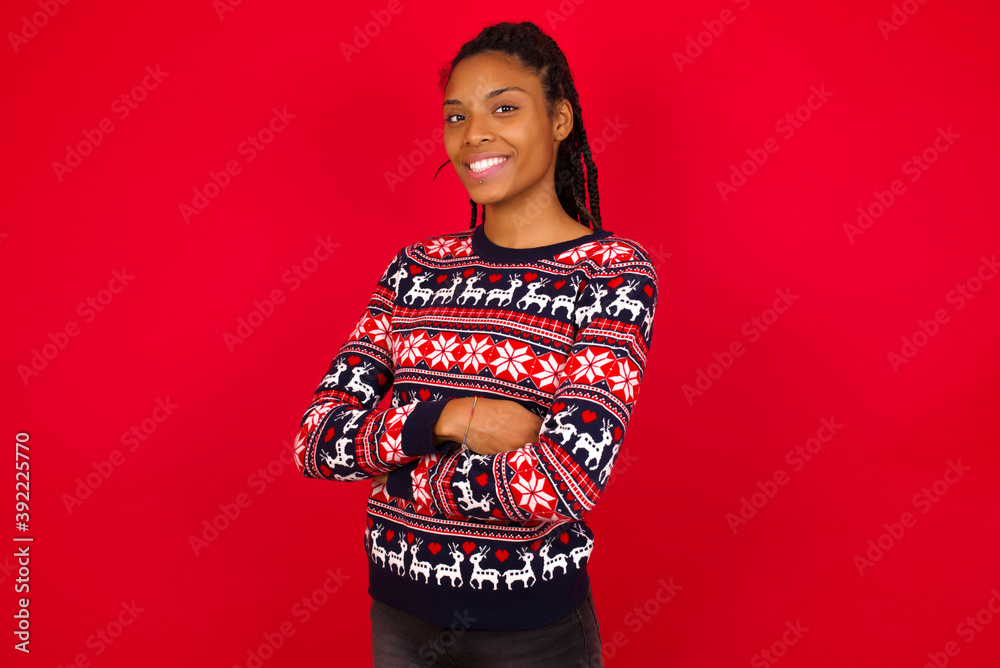 Young beautiful African American woman standing against red background happy face smiling with crossed arms looking at the camera. Positive person. Young beautiful African American woman standing against red background happy face smiling with crossed arms looking at the camera. Positive person.