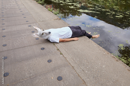 A man wearing a dog mask lies on a canal tow path photo