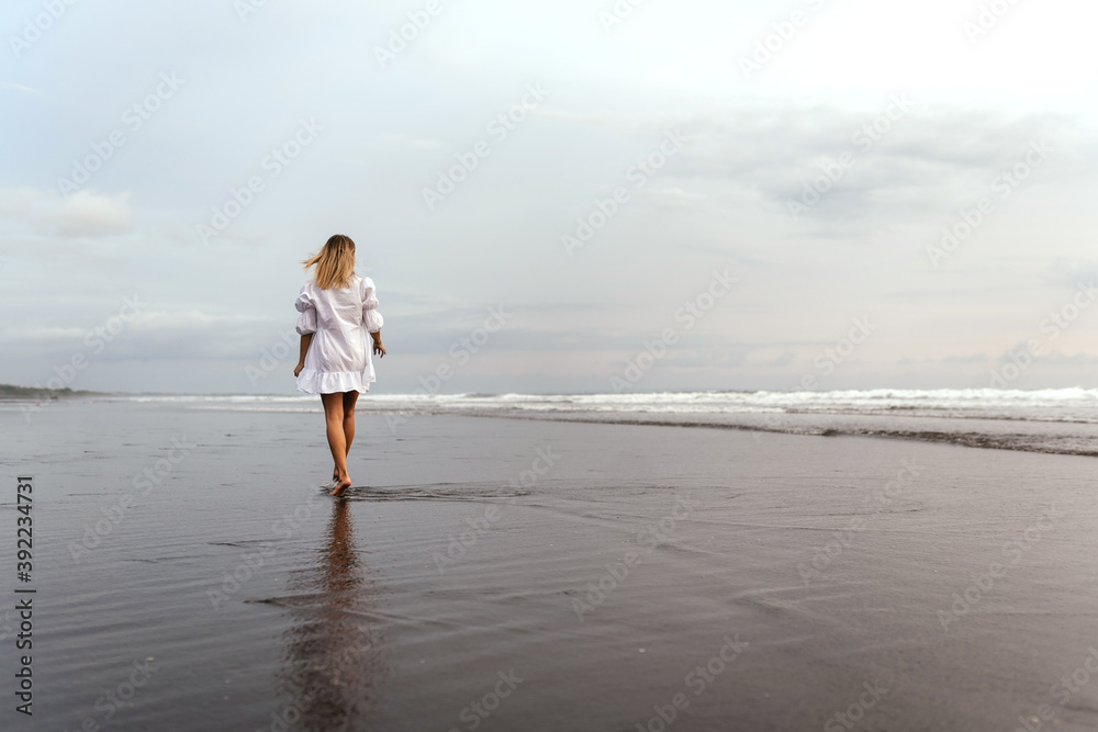 young woman wearing beautiful white dress is walking on the beach during sunset. Bali Indonesia