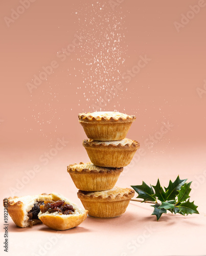Mince pies stacked on each other on pink background with sugar sifting on top. A mince pie is a traditional Christmas sweet pie, filled with a mixture of dried fruits and spices.