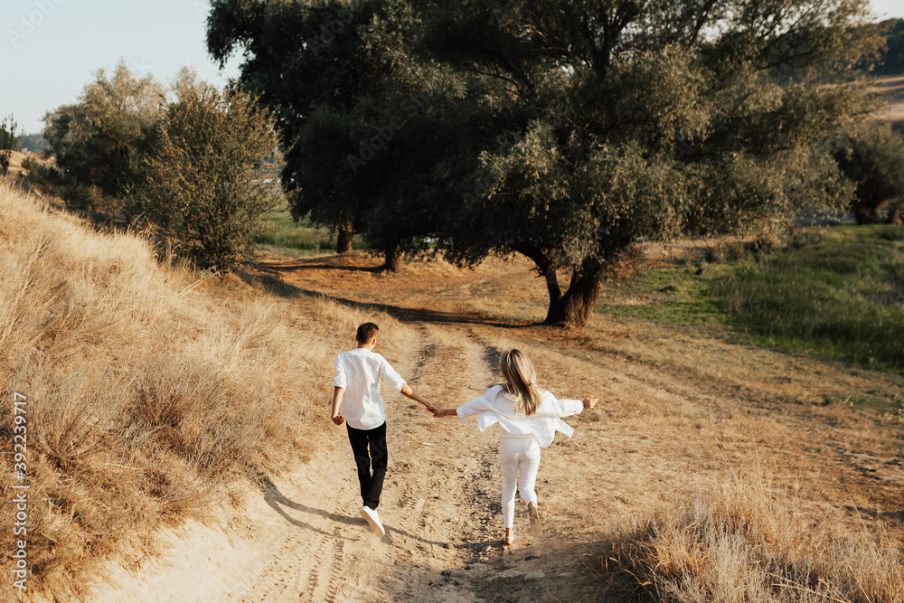 Back of young couple in love is holding hands, running, having fun and enjoying the beautiful nature in the park. Back of young couple in love is holding hands, running, having fun and enjoying the beautiful nature in the park.