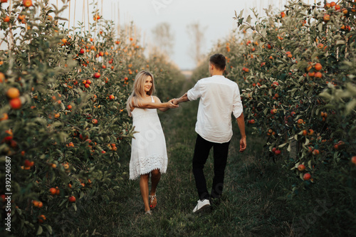 Obraz na płótnie Two lovers in nature. Woman in white dress holding hand of man following her. She is smiling happily. w salonie
