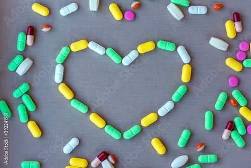 Heart shape outline lined with pills of different colors on gray textile background. Tablets are scattered around
