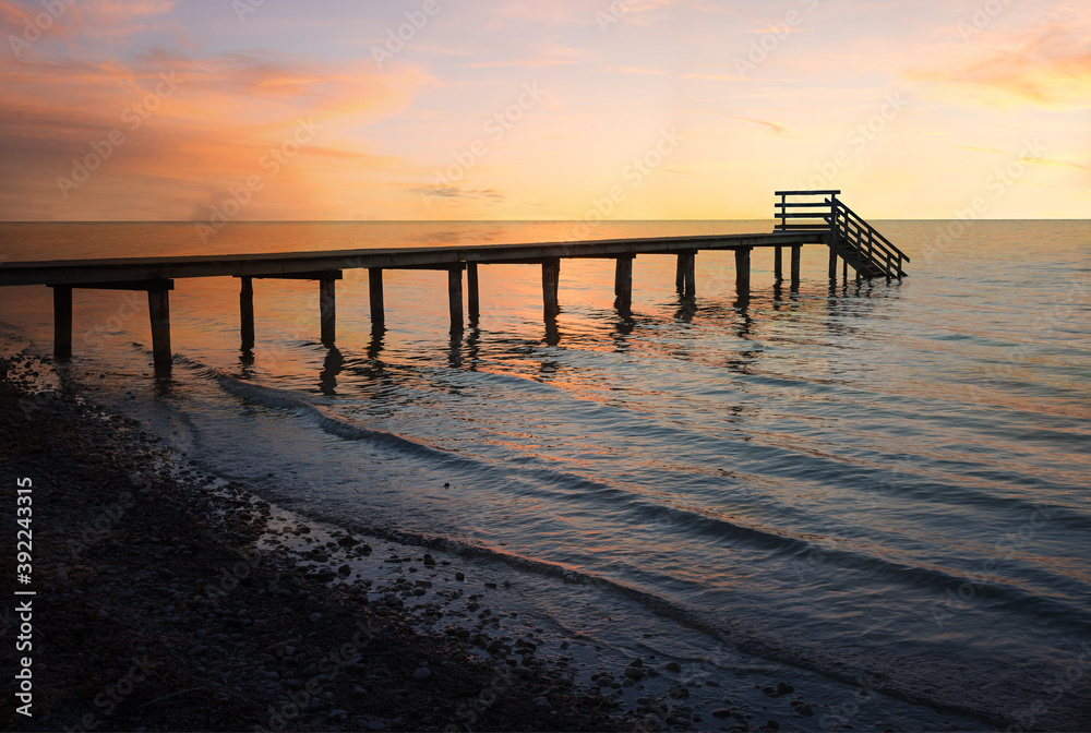 dreamy sunset scenery at stony beach with wooden boardwalk and waves