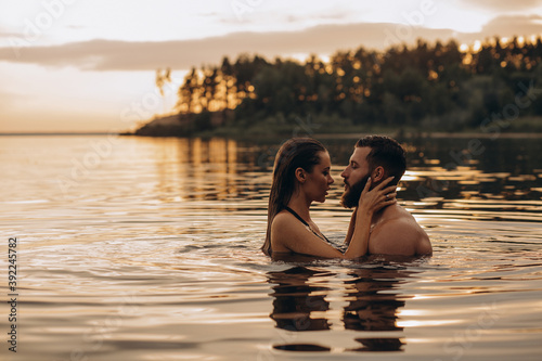 Romantic photo session in the water. A guy and a girl swim in the lake in the evening. Beautiful sunset.
