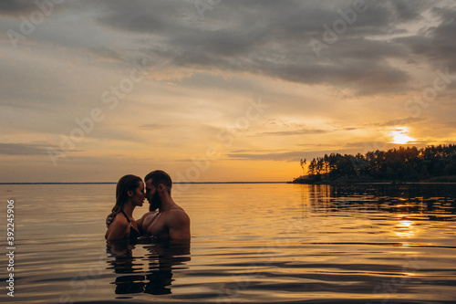 Romantic photo session in the water. A guy and a girl swim in the lake in the evening. Beautiful sunset. © dimadasha