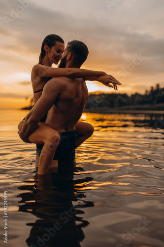 Romantic photo session in the water. A guy and a girl swim in the lake in the evening. Beautiful sunset.