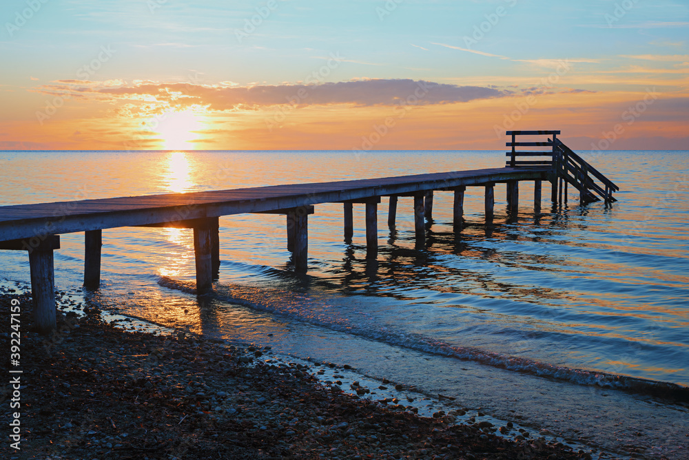 romantic sunset scenery at stony beach with wooden boardwalk and waves