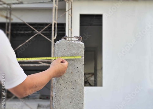 Yellow tape measure, concrete columns, reinforced concrete fence posts. Construction background worker white coat of arms asian background