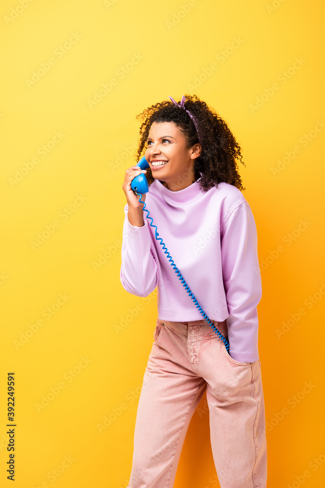 happy african american woman talking on blue retro phone on yellow happy african american woman talking on blue retro phone on yellow