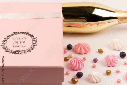 pink gift box with scattered multicolored sweets and bizet cake on a white wooden table