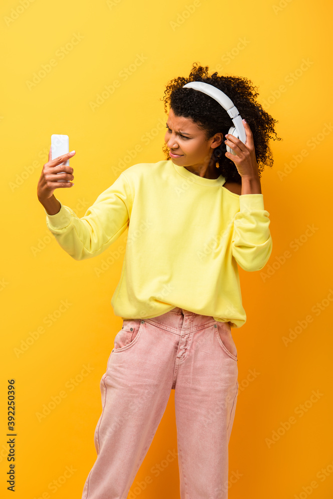 dissatisfied african american woman in headphones holding smartphone on yellow dissatisfied african american woman in headphones holding smartphone on yellow