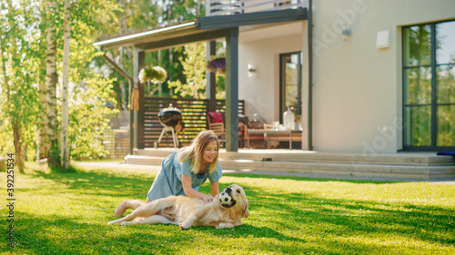 Cute Girl Has fun with Happy Golden Retriever Dog on the Backyard Lawn. She Pets, Play, Tackle it on the Ground And Scratches Back. Happy Dog Plays with Toy Ball. Idyllic Summer House.