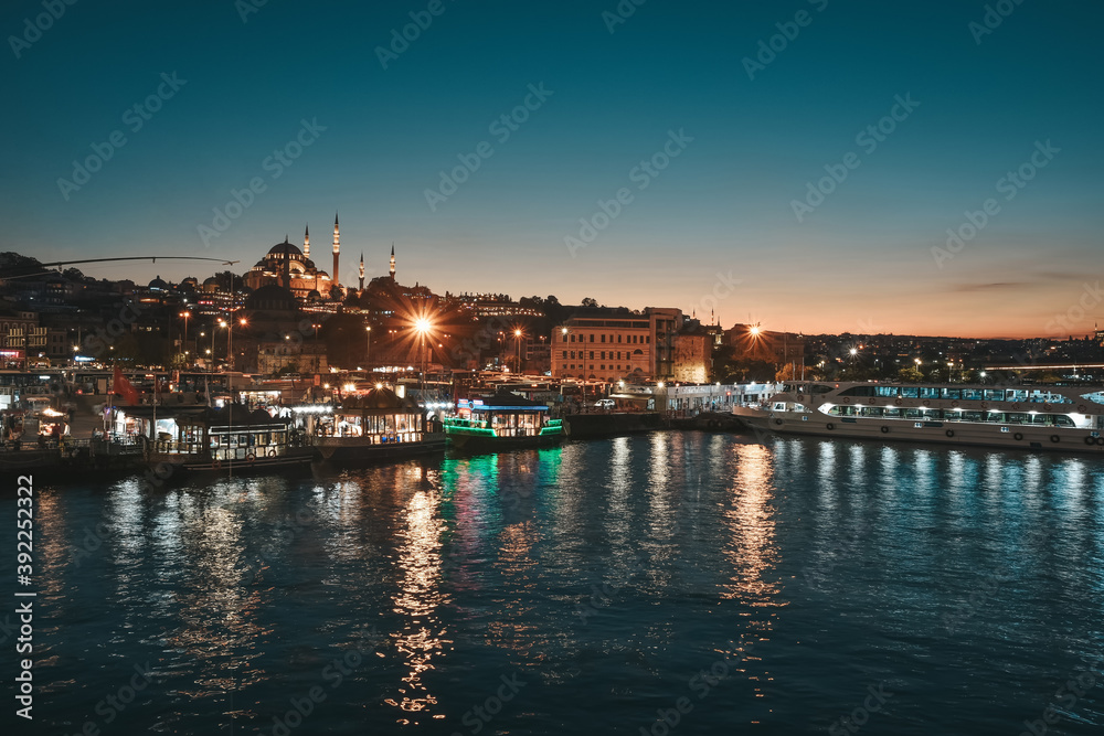 Night view on the restaurants at the end of the Galata bridge, Sultanahmet, at sunset with the famous Suleymaniye Mosque in the background, Istanbul, Turkey,