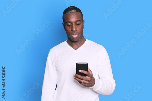 Cheerful African American man in white sweater using mobile phone application. © 2Design