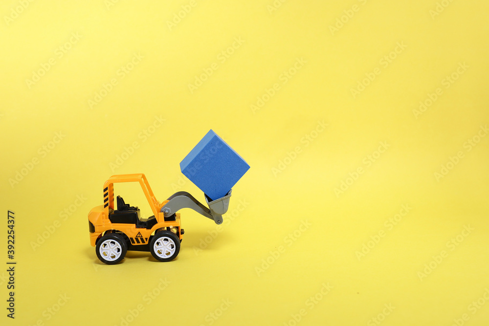 A toy bulldozer lifting a cube on yellow background A toy bulldozer lifting a cube on yellow background