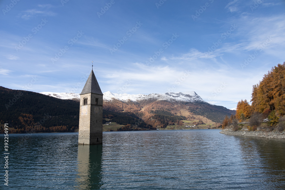 Famous submerged church steeple arising from the alpine Resia Lake, in the town of Curon Venosta, in the italian Dolomite region of Trentino Alto Adige. Scenic view.