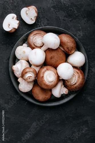 Fresh organic brown and white champignon mushrooms in bowl on dark stone background.