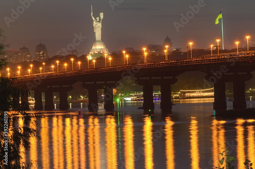 Autumn night cityscape with Paton bridge over Dnieper river. Motherland monument at the background. City lights reflected in the water. Kyiv, Ukraine