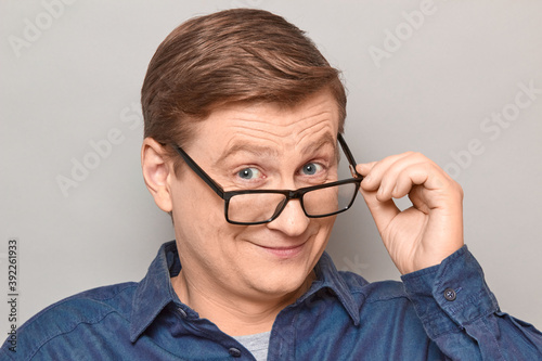 Portrait of happy blond mature man looking over his glasses at you