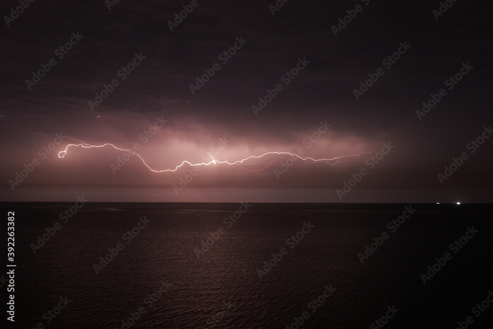 Thunderstorm with lightning over the sea at night. Lightning flashes and storm clouds