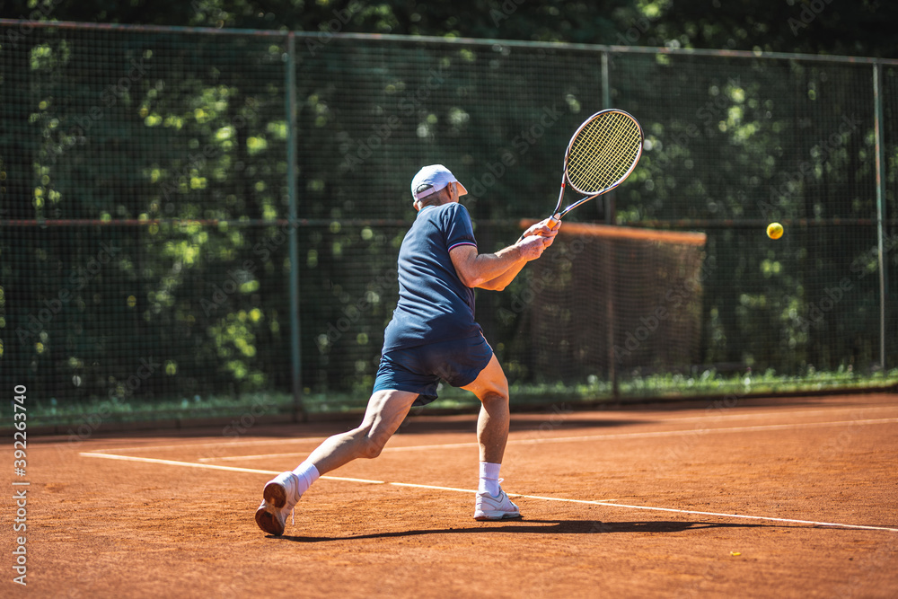 Active senior Caucasian man in sportswear playing tennis, steps forward and hits a ball