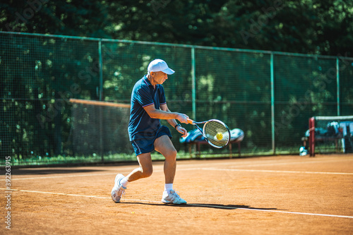 Active senior Caucasian man in sportswear playing tennis, hits a ball