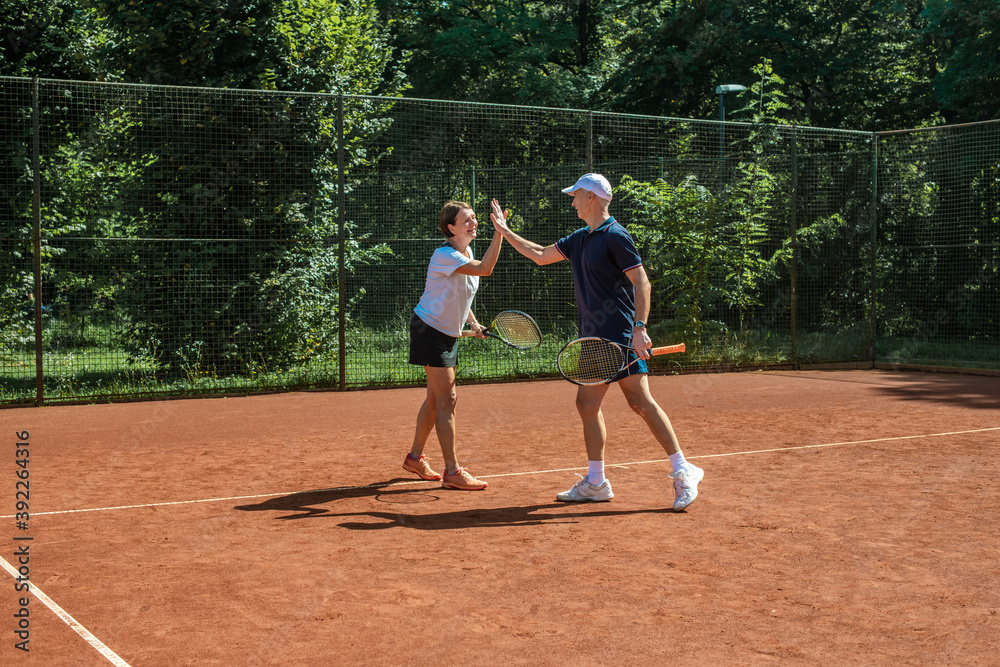 Active senior Caucasian couple in sportswear playing tennis, giving a high five to each other