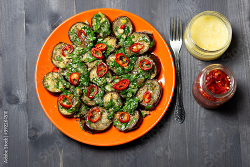 Eggplant salad with herbs and spices on red plate on black wooden background