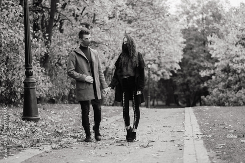 Young red haired woman puts on face mask while walking with young man in autumn park.