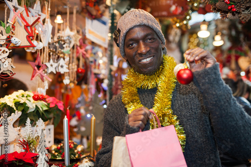 Portrait of smiling African American man with shopping bags on festive fair before Christmas.