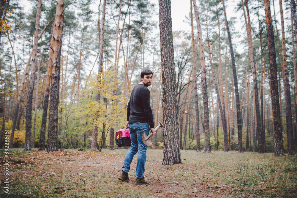 Theme is death of pet. Rear view of man walking along forest path and carrying shovel in one hand for digging grave, and in other transport box with an animal inside. The last path of cat Theme is death of pet. Rear view of man walking along forest path and carrying shovel in one hand for digging grave, and in other transport box with an animal inside. The last path of cat