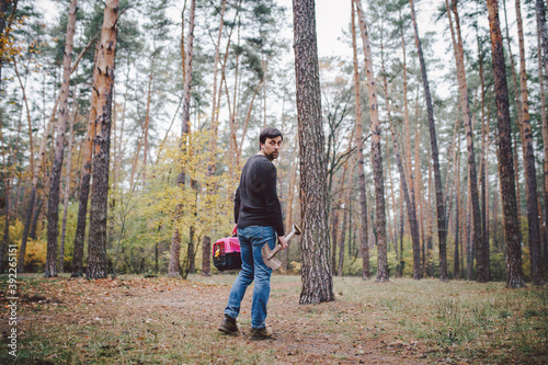 Theme is death of pet. Rear view of man walking along forest path and carrying shovel in one hand for digging grave, and in other transport box with an animal inside. The last path of cat