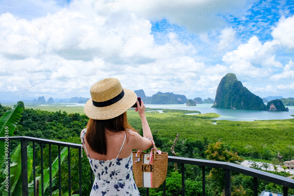 Happy Young Traveler Woman Raised Arm take a photo To Sky Enjoying A Beautiful Of Nature Samed Nang Chee on mountain landscape view point at jame bond island seascape at Antaman sea in thailand. 