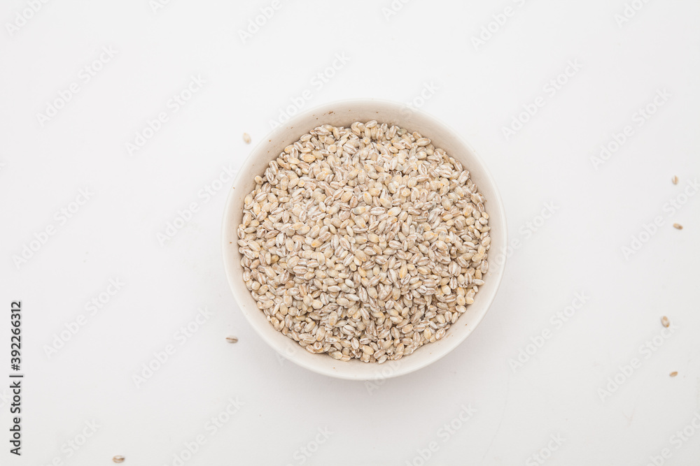 Unhulled barley in white bowl on white background Unhulled barley in white bowl on white background