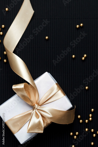 Gift with a ribbon on a black textured background. Gold beads on a black background. Festive background. Christmas and New Year background. Greeting card with a gift. Stylish gift concept. Free space.