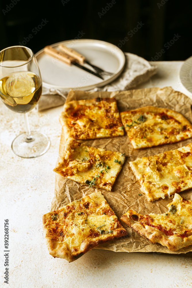 Homemade Belgian style four cheeses pizza, flammekeuche, on wooden board, glass of white wine 