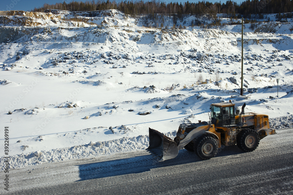 Wheeled front-end loader moves along the road in a snow-covered stone quarry, close-up. Wheeled front-end loader moves along the road in a snow-covered stone quarry, close-up.