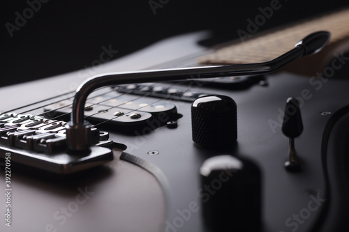 Elegant electric guitar on black background close up point of view of body details with black knobs and humbucker pickups to last frets with silver tremolo and black pickguard