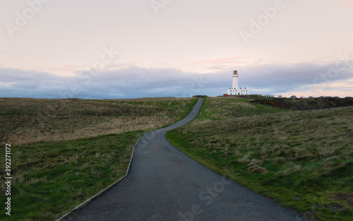 Lighthouse under bright sky with grasses and road in foreground, Flamborough, UK.