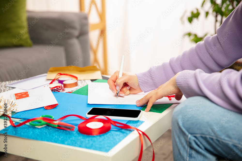 Close up female hands making greeting card for New Year and Christmas 2021 for friends or family, scrap booking, DIY. Writing a letter with best wishes, design her homemade card. Holidays, celebration Close up female hands making greeting card for New Year and Christmas 2021 for friends or family, scrap booking, DIY. Writing a letter with best wishes, design her homemade card. Holidays, celebration