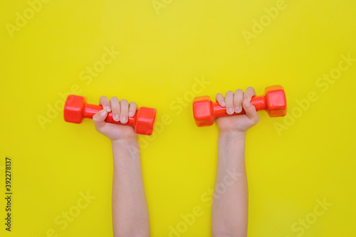 Children's hands hold red dumbbells on a yellow background.