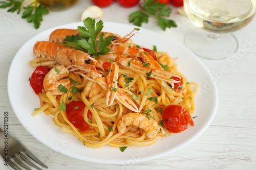 Italian Traditional Dish"Linguine agli Scampi" or "Linguine with Scampi Shirmps",linguine with scampi,cherry tomatoes,white wine,olive oil,parsley,garlics and peppers on white plate with white table
