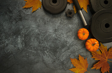 Heavy dumbbells weight plates with small decorative pumpkins and autumn leaves. Gym workout flat lay composition, healthy fitness lifestyle concept with copyspace.