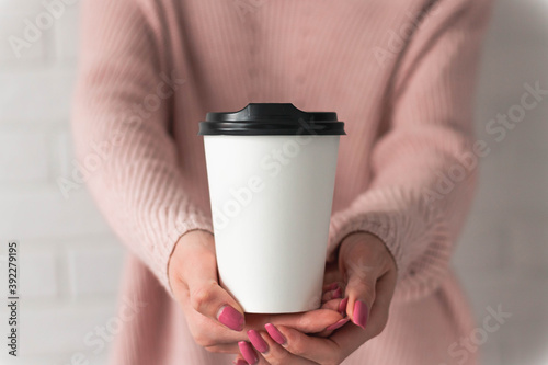 Girl holding white paper cup of takeaway coffee in the hand. Place for your text or log. Winter and Christmas time concept.
